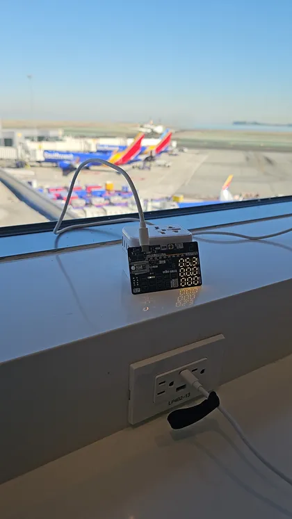 The Negotiator II plugged into a travel charger on an airport window ledge, with planes on the apron behind it