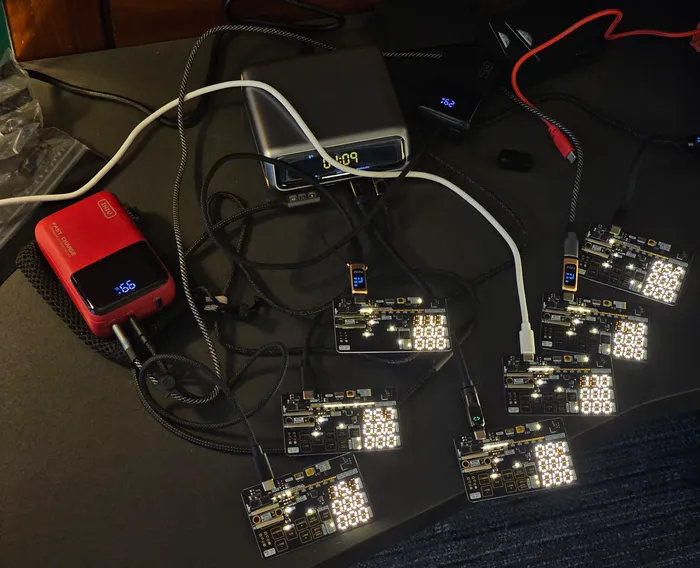 Seven Negotiator II cards lit up on a desk, each powered by its own USB charger or power bank
