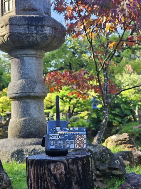 The Negotiator II on a power bank on a tree stump in a Japanese garden, a stone lantern and a red maple behind it