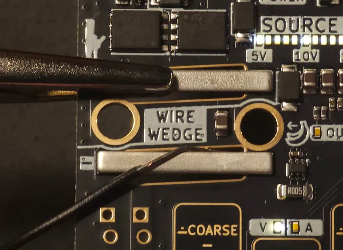 A crocodile clip on the top bar of the wire wedge and a wire wedged under the bottom bar, pulled along the board